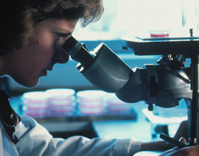 Científico usando un abrigo de laboratorio y mirando en un microscopio.