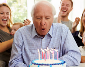 Foto de un anciano en una fiesta de cumpleaños soplando las velas de una tarta de cumpleaños.
